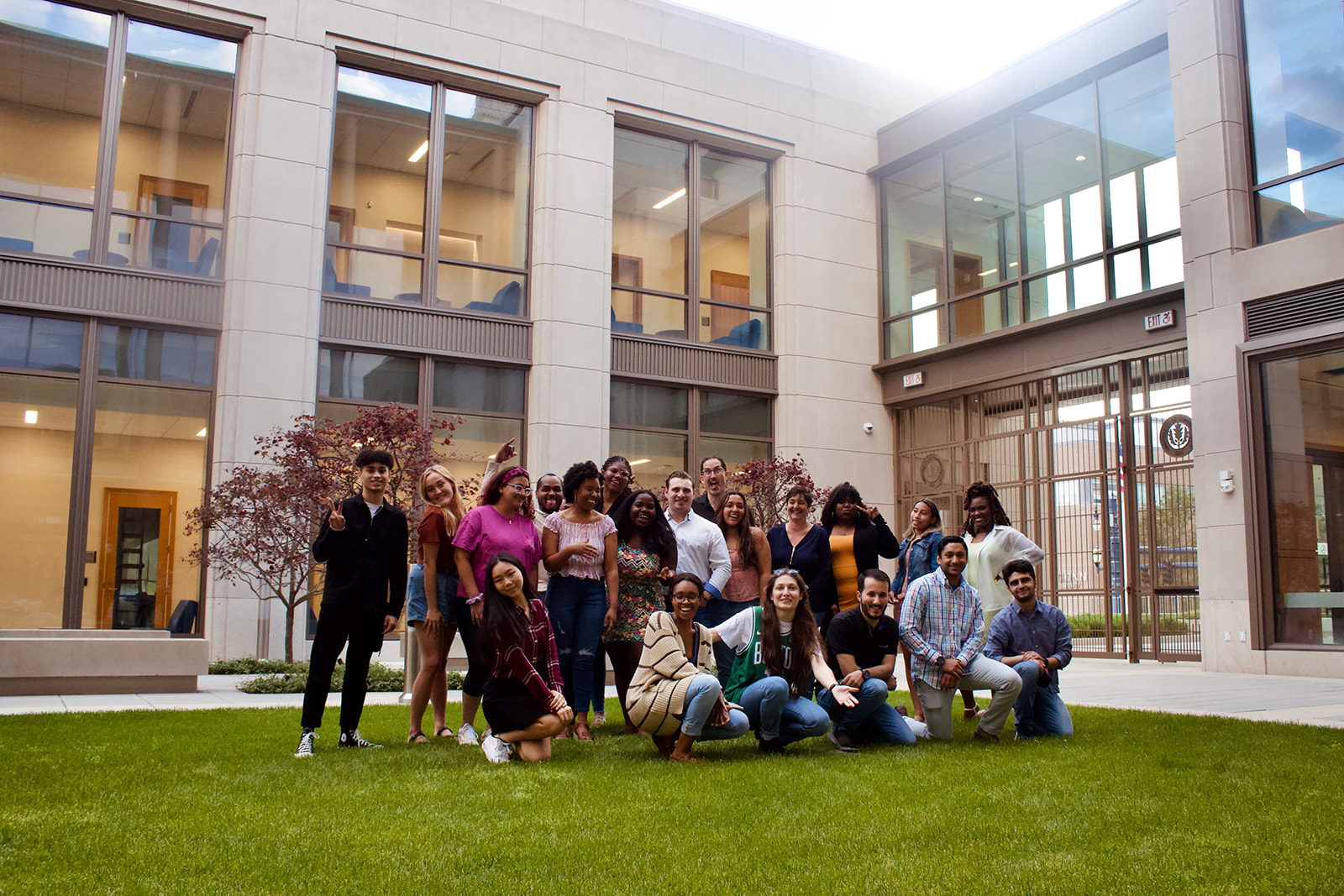 Image shows the group of students and staff standing and kneeling on the grass in the campus courtyard.