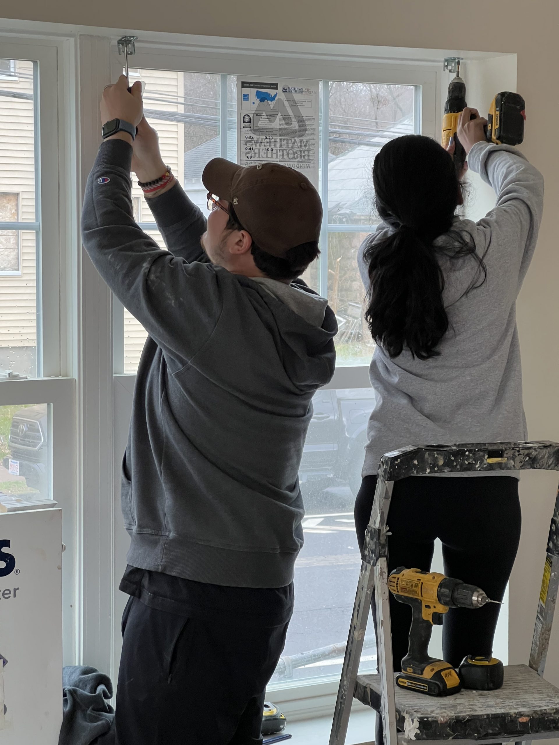 Two students installing blinds onto window.